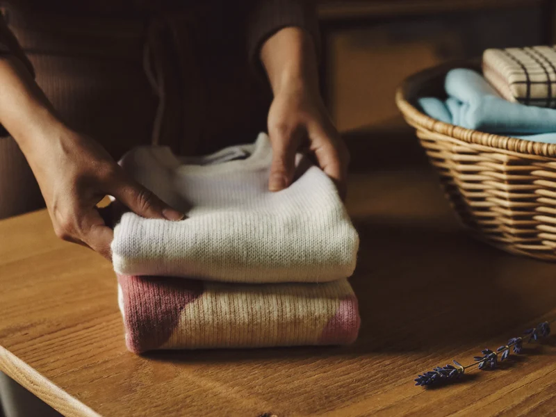 Forældrehænder folder en lille sweater ved en kurv med nyvasket børnetøj